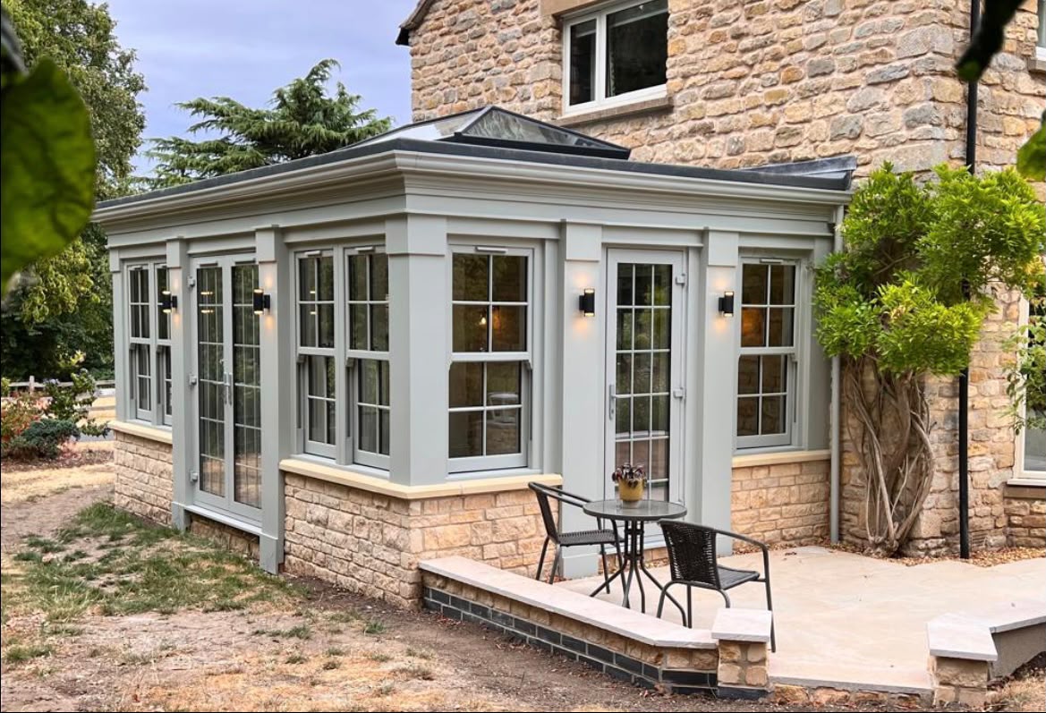Orangery with grey sash windows and French doors fitted to a stone house